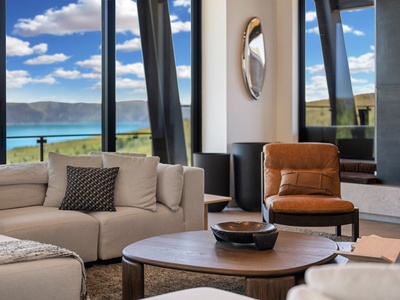 Relax in this stunning living room with floor-to-ceiling windows framing breathtaking lake and mountain views. Sink into plush sofas and soak in the serene, sunlit beauty of your private escape.