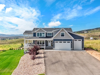 Modern two-story home with covered porch and attached garage, surrounded by expansive mountain views and open grassland.