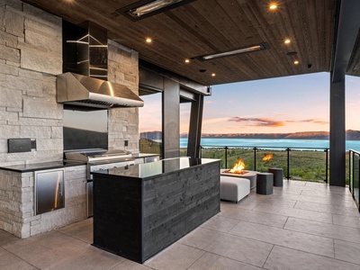 Modern outdoor kitchen with a sleek cooking setup and fire feature, all framed by breathtaking lake and mountain sunset views—ideal for memorable evenings under the stars.