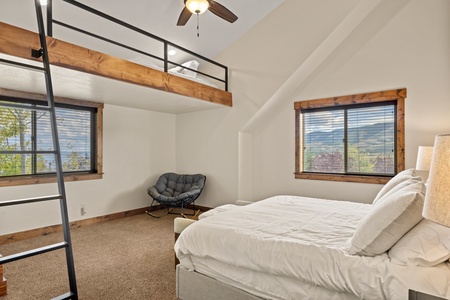 Wake up to mountain views framed by wooden accents and cathedral ceilings. Your cozy bedroom features a lofted sleeping nook, plush seating, and natural light streaming through large windows—a peaceful retreat in nature.