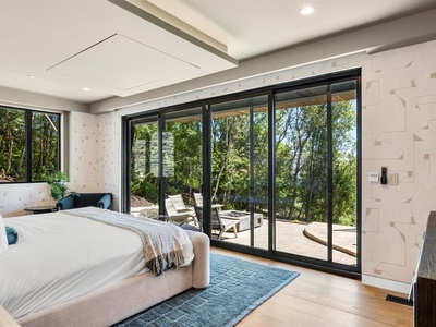 Relax in your sun-filled bedroom where crisp linens and floor-to-ceiling glass doors open to your private terrace surrounded by lush greenery, creating your perfect peaceful retreat.