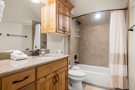 Your private bathroom features warm wood cabinetry, soft granite countertops, and a pristine tub-shower combo—fresh towels and toiletries ready for your arrival.