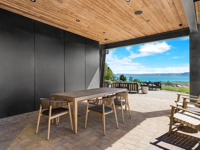 Covered patio frames sweeping views of turquoise waters and distant mountains, perfect for al fresco dining beneath warm wood ceilings and modern finishes.