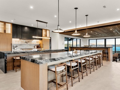Gather around the stunning island with sweeping water views framed by expansive windows. Natural wood tones, sleek marble counters, and modern pendant lighting create a warm yet sophisticated space for your group meals and conversations.