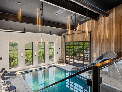 An elegant indoor pool with warm ambient lighting and modern design invites you to unwind. Floor-to-ceiling windows frame garden views, while sleek loungers await your relaxation.