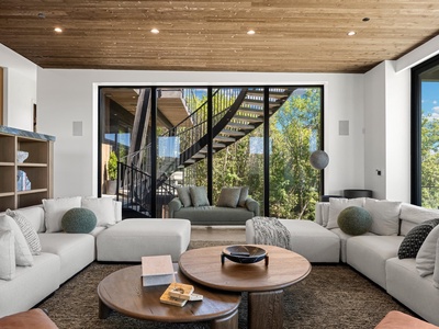 Sink into plush sofas as warm wood ceilings embrace you above. Floor-to-ceiling windows frame lush greenery, inviting nature into your modern retreat while natural light floods every corner.