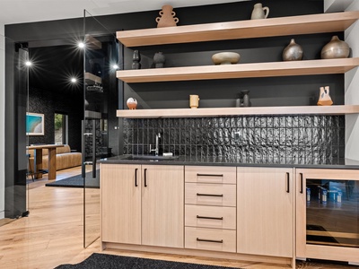 Prepare meals in your sleek kitchenette featuring light wood cabinetry, textured black tile, and open shelving for a modern, functional touch.