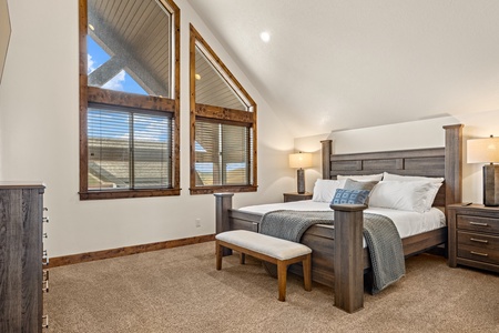 Sink into your plush bed beneath vaulted ceilings and natural light streaming through tall windows, all framed by warm wood accents that make this serene retreat feel like home.