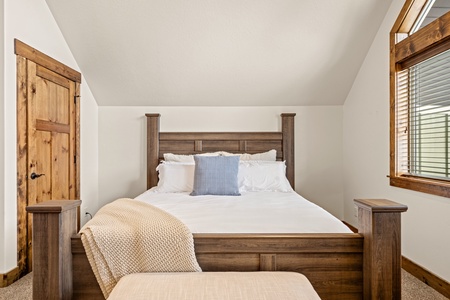 Cozy up in this inviting bedroom featuring a rustic wooden bed dressed in soft linens, perfectly complemented by warm wood accents and peaceful natural light.
