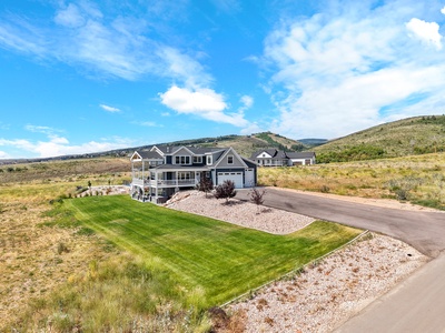 Expansive property nestled in rolling hills with manicured lawn and mountain backdrop under bright blue skies.