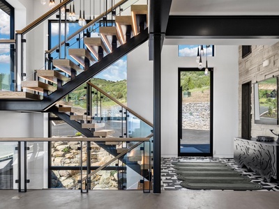 Modern mountain retreat entrance welcomes you with soaring ceilings, an architectural staircase, and sweeping natural views—your peaceful escape awaits beyond these doors.