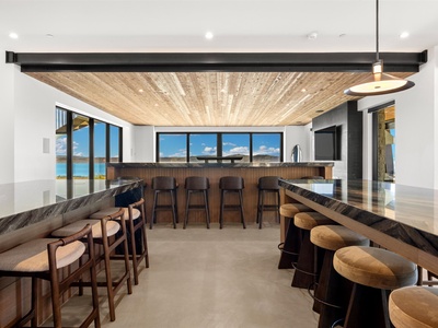Picture yourself gathering at this stunning bar, where modern design meets natural warmth under a beautiful wood-paneled ceiling. Large windows frame breathtaking lake views, creating the perfect backdrop for your morning coffee or evening drinks.