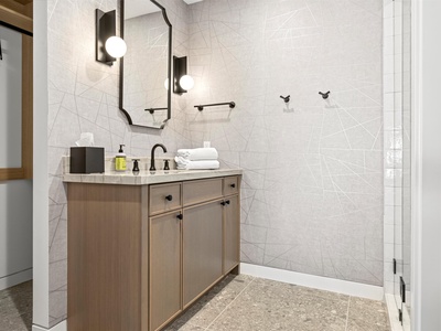 Your private bathroom features elegant marble-style tiles, warm wood cabinetry, and modern black fixtures. Fresh towels and thoughtful amenities await your arrival.