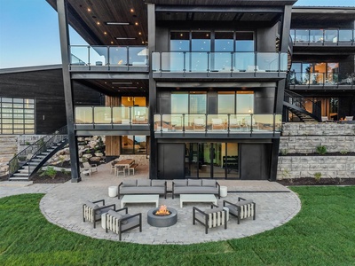 This striking modern property features expansive glass terraces, dramatic architectural lines, and an elegant circular firepit patio perfect for cool evenings under the stars.