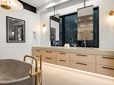 Your private spa-like retreat features a soaking tub, dual vanities, and forest views through floor-to-ceiling windows. Elegant lighting and warm wood finishes create a serene escape for unwinding.