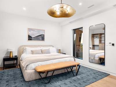 Sink into crisp linens and natural textures in your serene bedroom retreat. A statement brass fixture casts warm light over your restful sanctuary with mountain views.