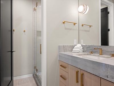 Step into your serene spa-like bathroom with elegant marble vanity, gold fixtures, and a refreshing walk-in shower with stylish tile work—fresh towels await your arrival.