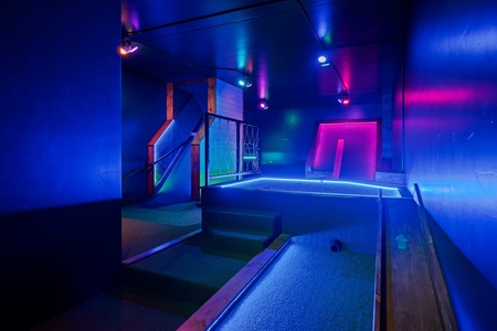 Your private indoor mini golf course glows with vibrant neon blues and pinks, creating a futuristic playground perfect for friendly competition and unforgettable evenings.
