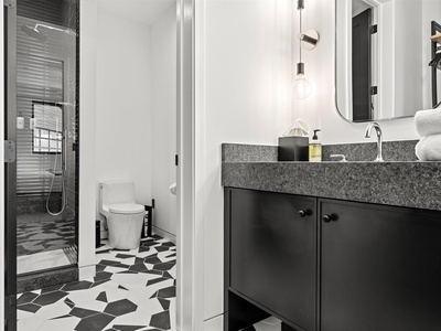Step into your sleek modern bathroom with striking geometric floors, granite countertops, warm pendant lighting, and a glass-enclosed rainfall shower—designed for your comfort and style.