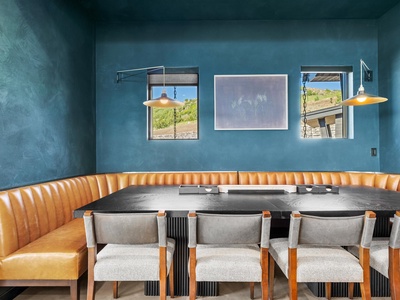 Gather around this striking dining area where modern design meets warmth—bold blue walls, soft ambient lighting, and desert views set the scene for memorable meals together.