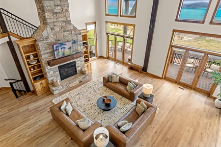 Sink into plush leather seating beneath soaring ceilings as turquoise waters shimmer through floor-to-ceiling windows, and the stone fireplace adds rustic warmth to your lakeside retreat.