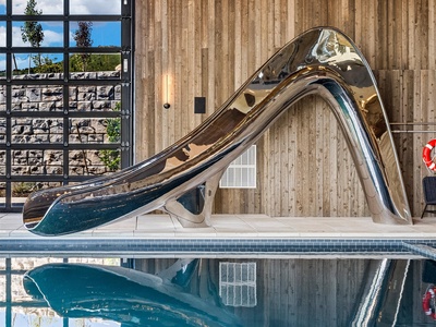 A stunning metallic slide curves gracefully into the indoor pool, promising thrilling moments during your stay. Natural light streams through floor-to-ceiling windows, illuminating the warm wood-paneled walls and creating a perfect retreat for fun and rel
