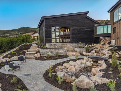 Modern mountain retreat featuring dark wood architecture, terraced stone landscaping, and serene outdoor spaces nestled in a hillside setting with scenic valley views.