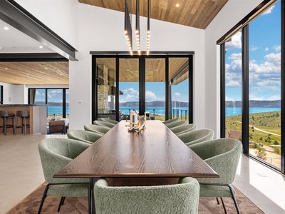 Gather around this stunning dining table where every meal becomes a memory, framed by panoramic water and mountain views through floor-to-ceiling windows that flood the space with natural light.