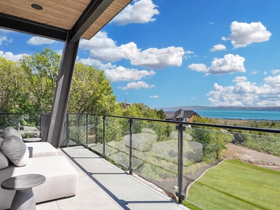 Sip your morning coffee on this covered balcony with sweeping lake views, plush outdoor seating, and a peaceful garden below—your private escape to unwind and soak in the scenery.