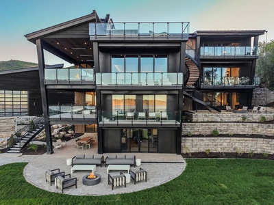 Modern architectural luxury property with multiple levels, glass railings, rooftop terraces, and outdoor fire pit seating overlooking rolling hills—a stunning vacation home with contemporary design and expansive entertaining spaces.