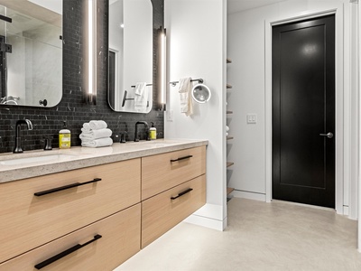Step into your sleek, modern bathroom with its striking black subway tile accent wall, spacious double vanity, and soft towels waiting just for you.