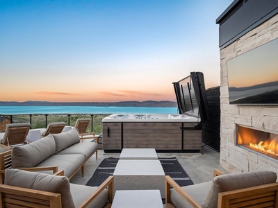 Unwind on your private rooftop terrace with a hot tub, outdoor fireplace, and sweeping lake views framed by distant mountains at sunset.