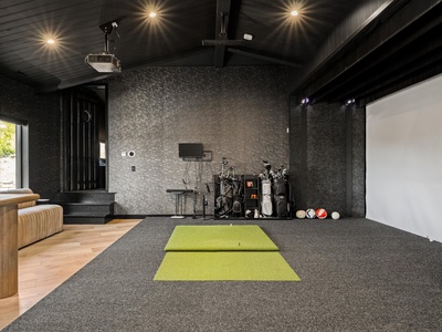 Practice your swing in this private golf simulator room with projection screen, textured walls, and natural light filtering through when you need a break.