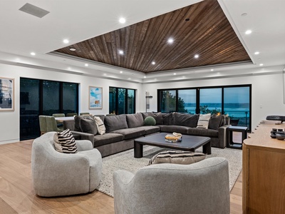 Settle into this expansive living space where dramatic wood ceilings and floor-to-ceiling windows frame stunning water views—your perfect gathering spot after a day exploring.