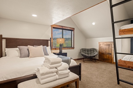 Sink into crisp linens and rest easy in your mountain retreat. Vaulted ceilings and warm wood accents create a cozy sanctuary, while a glimpse of the surrounding landscape frames your peaceful escape.