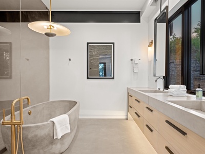 Indulge in your private spa-like retreat with a stunning concrete soaking tub, elegant brass fixtures, and serene views framing your peaceful escape.