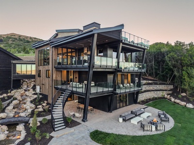 Modern architectural retreat set against mountain backdrop, featuring expansive glass balconies, natural stone landscaping, and inviting outdoor living spaces perfect for gatherings.