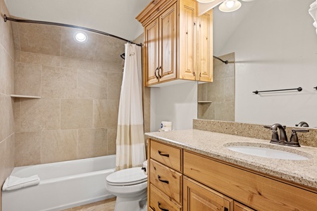 Step into your private bathroom featuring warm wood cabinetry, granite countertops, and a relaxing tub-shower combo with elegant tile surrounds and built-in storage niches.