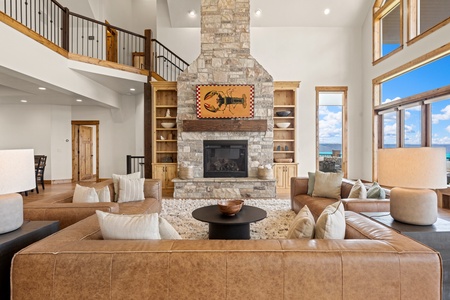 Relax by your stone fireplace in this soaring living space, where floor-to-ceiling windows frame breathtaking lake views and warm leather seating invites you to unwind in style.