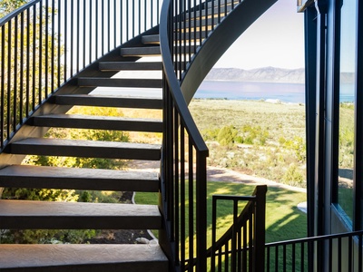Modern outdoor staircase leads to stunning lake and mountain scenery framed by natural desert landscape and manicured lawn.