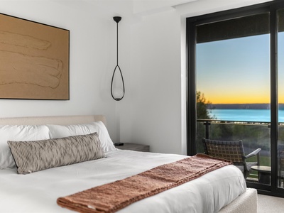 Wake up to serene waterfront views framed by your bedroom window. This peaceful retreat features a cozy bed, modern design, and stunning sunset vistas over the lake—your perfect escape awaits.