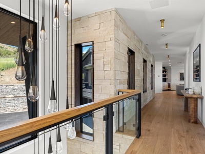 Modern stone hallway with dramatic pendant lighting and warm wood flooring connects your stylish living spaces. Natural light pours through floor-to-ceiling windows, illuminating the elegant interior finishes.