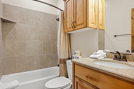 Step into your private bathroom with warm wooden cabinetry, granite countertops, and fresh towels waiting. The tiled tub-shower combo offers a refreshing retreat after your mountain adventures.