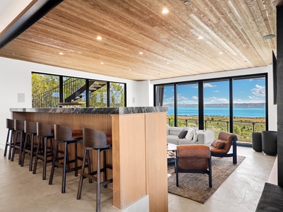 Imagine unwinding in this open-concept living space where warm wood tones meet panoramic lake views. Gather at the sleek bar, sink into plush seating, and let natural light fill every corner of your retreat.