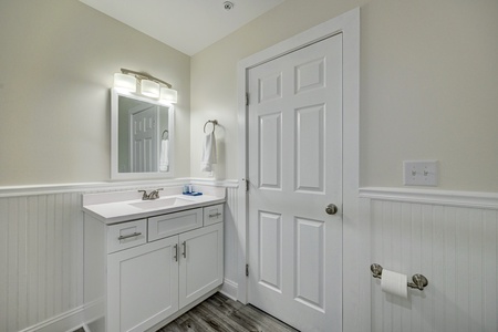 Relax in your spotlessly clean bathroom featuring fresh white cabinetry, elegant beadboard wainscoting, and bright vanity lighting for your morning routine.