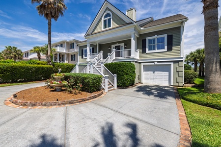 Charming coastal property featuring classic architecture with a welcoming front porch, mature palm trees, and manicured landscaping that create a peaceful retreat for your vacation stay.