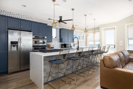 Your spacious kitchen invites culinary adventures with sleek navy cabinets, marble island seating, and ocean views through bright windows.