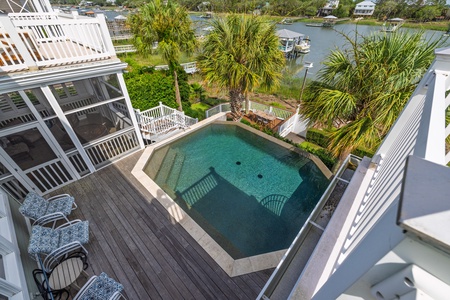The property features a distinctive geometric pool surrounded by tropical landscaping and waterfront access, with boats docked along the scenic canal and neighboring homes dotting the shore.