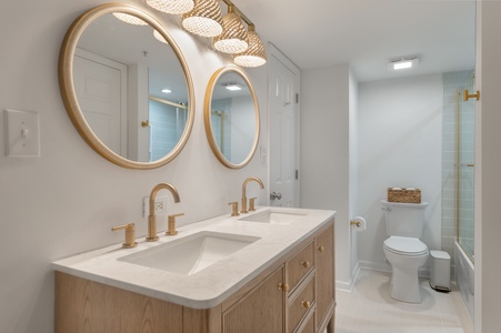 Pamper yourself in this spa-like bathroom featuring dual vanities, gold fixtures, and a stunning glass-tiled shower.