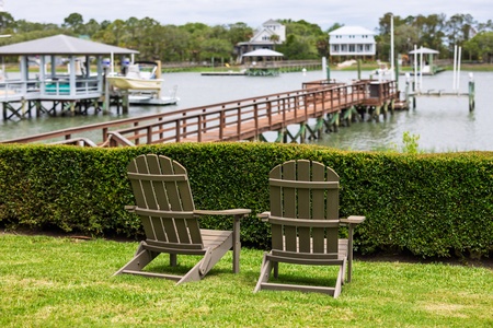 A serene waterfront property along a calm river, featuring a private dock and manicured lawns. Nearby homes visible across the water.